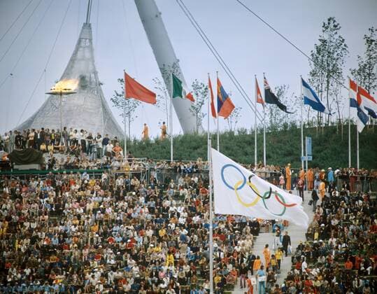 Eröffnungsfeier der Olympischen Spiele 1972 in München: Das Olympische Feuer brennt oberhalb der Zuschauer neben den Nationalfahnen der Teilnehmerländer