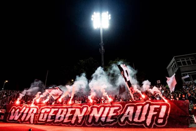 Fussball, Saison 2025 2026, 3. Liga, Donaustadion Ulm, 7. Spieltag, SSV Ulm 1846 Fußball - SSV Jahn Regensburg, 21.09.2025 21.09.2025, Fussball, Saison 2025 2026, 3. Liga, Donaustadion Ulm, 7. Spieltag, SSV Ulm 1846 Fußball - SSV Jahn Regensburg, Die Fans des SSV Ulm im Fanblock Heimblock D-Block Donaustadion mit einem Banner WIR GEBEN NIE AUF! mit Pyrotechnik Pyro Foto: Lucca Fundel Ulm Donaustadion Baden-Württemberg Deutschland