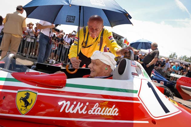 Formel 1 - GP Österreich Der ehemalige österreichische Formel-1-Rennfahrer und Weltmeister Niki Lauda (1949 - 2019) sitzt am 22.06.2014 während der Legenden-Parade vor dem Großen Preis von Österreich 2014 auf dem Red Bull Ring in Spielberg (Steiermark) am Steuer seines Ferrari 312 T2. Sein Chefmechaniker aus der Zeit, der Italiener Ermanno Cuoghi, hält ihm den Schirm. Dies ist das berühmte Modell, mit dem Lauda 1976 und 1977 für Ferrari fuhr und mit dem er 1977 seinen zweiten Weltmeistertitel gewann. Es ist einer der bekanntesten und erfolgreichsten Formel-1-Wagen der 70er Jahre.