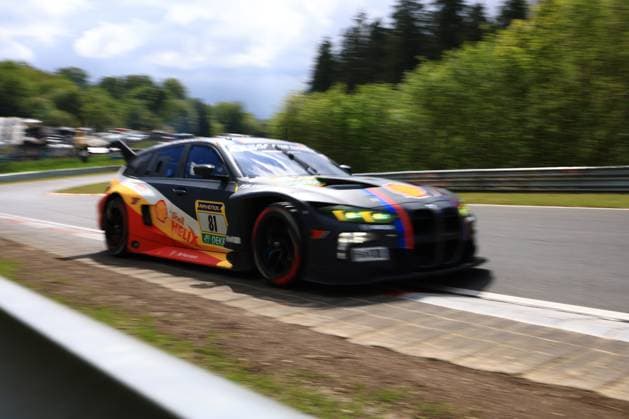 Das Jens Klingmann & Ugo de Wilde (Schubert Motorsport) von Schubert Motorsport durchfährt mit hoher Geschwindigkeit eine Kurve auf dem Nürburgring. Der BMW M4 GT3 trägt eine markante schwarz-gelb-rote Livery mit Shell Helix- und RAVENOL-Sponsoring sowie den charakteristischen BMW-Farben Blau und Rot als Akzentstreifen. Die grün leuchtenden Scheinwerfer und die roten Bremssättel verleihen dem Fahrzeug einen prägnanten Look. Die Panning-Aufnahme unterstreicht die Dynamik des Einsatzfahrzeugs beim ADAC RAVENOL 24h Nürburgring 2026. BMW M4 GT3 81 von Schubert Motorsport auf dem Nürburgring Copyright: xMichaelxGelhardtx