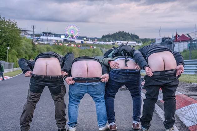 Vier Fans präsentieren am Nürburgring einen klassischen Mooning -Moment direkt auf dem Asphalt der Rennstrecke. Im Hintergrund ist das beleuchtete Riesenrad des Fahrerlagers sowie die Infrastruktur des Eventgeländes zu erkennen. Die ausgelassene Stimmung spiegelt die einzigartige Atmosphäre des 24h-Rennwochenendes wider. Fans zeigen ihren Hintern auf der Strecke am Nürburgring Copyright: xMichaelxSchäferx