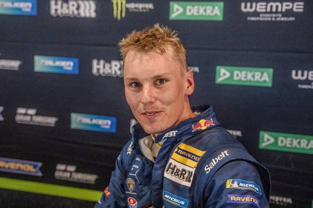 Luca Engstler vom Red Bull Team ABT steht vor der Pressewall des 24h Nürburgring. Der Fahrer trägt seinen Rennoverall mit Sponsoren wie RAVENOL, H&R und Michelin. Im Hintergrund sind die Logos von DEKRA, Falken, Monster Energy und Wempe zu sehen. Luca Engstler beim 24h Nürburgring 2026 im Fahrerlager Copyright: xMichaelxSchäferx