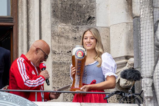 Munich, Bavaria, Germany May 17, 2026: Soccer: FC Bayern Munich™s championship celebration on the City Hall balcony and at Marienplatz in Munich following their victory in the 2025 2026 Bundesliga season. A woman in a dirndl holding an oversized PAULANER beer glass (Paulaner Brewery, Munich) next to stadium announcer Stephan Lehmann