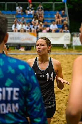 Eine Spielerin des niederländischen Nationalteams ( 14; NED) steht auf dem Sandfeld und spricht mit Mitspielern. Im Hintergrund sind Zuschauer auf blauen Tribünensitzen zu sehen. Niederländische Spielerin ( 14; NED) im Gespräch beim Beach-Handball
