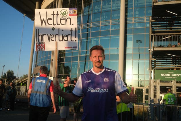 08.08.2026 Fußball Herren 2026 2027 2. Bundesliga 1. Spieltag VfL Wolfsburg - 1. FC Kaiserslautern Volkswagen Arena Wolfsburg Thomas Melchior, auch bekannt als der Sportwettensheriff auf Instagram, steht im Trikot des VfL Osnabrücks und seinem Schild Wetten Ihr verliert! vor der Volkswagen Arena, um auf die Gefahren von Sportwetten aufmerksam zu machen. Wolfsburg Niedersachsen Deutschland