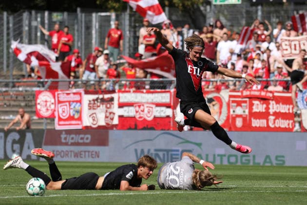 08.08.2026, xsefx, Fußball, FC Viktoria Köln SSV Jahn Regensburg, 3.Liga, Sportpark Höhenberg, 1. Spieltag, Saison 2026 2027: Tobias Eisenhuth (FC Viktoria Koeln 06) springt über den am Boden liegenden John Posselt (Jahn Regensburg 20) DFB regulations prohibit any use of photographs as image sequences and or quasi-video. Nordrhein-Westfalen Deutschland