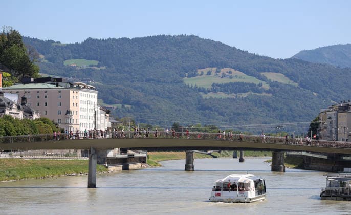 Österreich: Fußball UEFA Super Cup 2026, Finale, Paris Saint-Germain vs Aston Villa FC, Salzburg: Blick über die Salzach in Salzburg am Tag des UEFA Super Cup Finales 2026 zwischen Paris Saint-Germain und Aston Villa FC. Fußgänger überqueren eine Brücke, während ein Ausflugsschiff den Fluss passiert. Die Aufnahme zeigt die Atmosphäre der Gastgeberstadt vor dem internationalen Fußballereignis. Copyright: xAymanxAlahmedx
