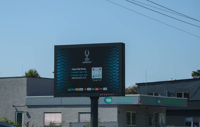 Österreich: Fußball UEFA Super Cup 2026, Finale, Paris Saint-Germain vs Aston Villa FC, Salzburg: Eine digitale Anzeigetafel wirbt in Salzburg für das UEFA Super Cup Fan Festival mit Veranstaltungszeiten und QR-Code. Die Aufnahme entstand am Spieltag des UEFA Super Cup Finales 2026 zwischen Paris Saint-Germain und Aston Villa FC und zeigt die Eventkommunikation im Stadtgebiet vor dem Anpfiff. Copyright: xAymanxAlahmedx
