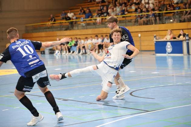 Magnus Holpert ( 22; VfL Lübeck-Schwartau) kämpft sich mit dem Ball durch die Abwehr von Grindstedt GIF und wird dabei von einem Gegenspieler gehalten. Nikolaj Svalastog ( 10; Grindstedt GIF) nähert sich von links, während Holpert in einer dynamischen Wurfvorbereitung tief in die Knie geht. Magnus Holpert ( 22; VfL Lübeck-Schwartau) im Zweikampf gegen Grindstedt GIF