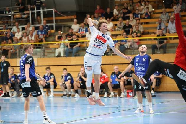 Magnus Holpert ( 22; VfL Lübeck-Schwartau) springt hoch und zieht zum Wurf ab, während Anders Toft ( 8; Grindstedt GIF) die Aktion beobachtet. Im Hintergrund verfolgen zahlreiche Zuschauer das Spiel in der Hansehalle Lübeck. Magnus Holpert ( 22; VfL Lübeck-Schwartau) beim Sprungwurf in der Hansehalle