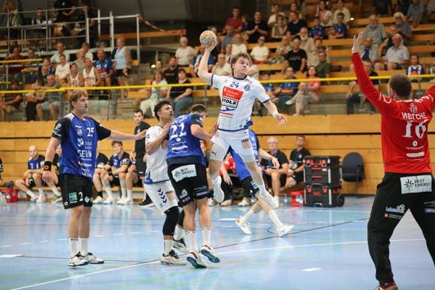 Alexander Hartwig ( 24; VfL Lübeck-Schwartau) zieht in der Hansehalle Lübeck hoch zum Sprungwurf, während Rune Overlund ( 25; Grindstedt GIF) und weitere Abwehrspieler von Grindstedt GIF unter ihm verteidigen. Rechts im Bild ist Christian Wetche ( 16; Grindstedt GIF) als Torwart positioniert. Alexander Hartwig ( 24; VfL Lübeck-Schwartau) beim Sprungwurf gegen Grindstedt GIF