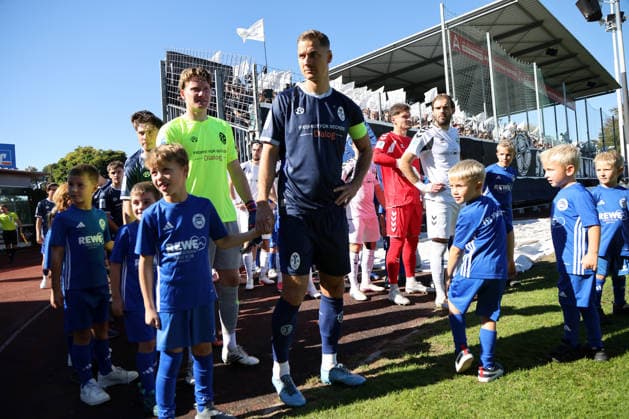 Fussball, Herren, Regionalliga Bayern, Saison 2026 2027, SV Wacker Burghausen - TSV 1860 München , flatbuy-Stadion an der Liebigstraße Die Mannschaften beim Einlaufen hier Paul Bachmann (TSV 1860 München) und Dennis Dressel (TSV 1860 München), rechts Felix Bachschmid (SV Wacker Burghausen)