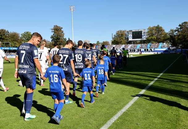 Fussball, Herren, Regionalliga Bayern, Saison 2026 2027, SV Wacker Burghausen - TSV 1860 München , flatbuy-Stadion an der Liebigstraße Die Mannschaften beim Einlaufen hier Paul Bachmann (TSV 1860 München) und Dennis Dressel (TSV 1860 München), rechts Felix Bachschmid (SV Wacker Burghausen)