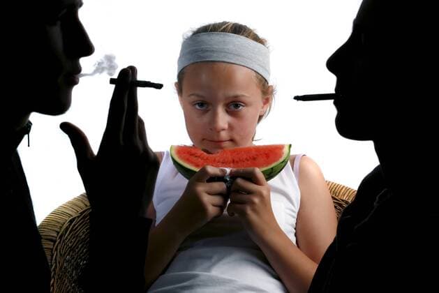 A Girl Eating a Watermelon with two adults smoking either side of her.