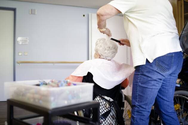 Eine Friseurin friesiert eine alte Frau im Rollstuhl in einem Pflegeheim, 27.04.2018, Berlin. NUR ZUR REDAKTIONELLEN VERWENDUNG. Berlin Deutschland