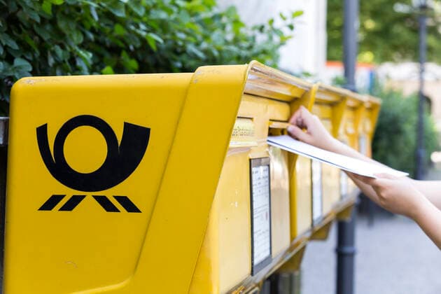 Frau steckt mehrere Brief in einen Briefkasten der Deutschen Post AG
