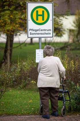 Schein - Bushaltestelle fuer Demenzkranke Eine Seniorin betrachtet am 29.10.2014 im Garten des Pflegecentrums Sonnenschein in Gerstungen ( Thueringen ) den Fahrplan an einem Bushaltestellenschild . Hier faehrt kein Bus - die Atrappe hilft, demenzkranke Bewohner vor einem Umherirren zu schuetzen. Gerstungen Thüringen DEUTSCHLAND