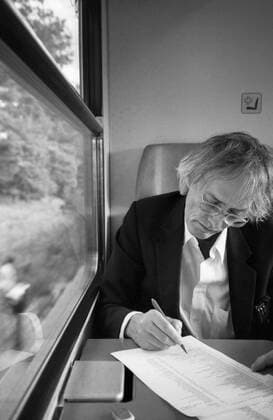 Timm Ulrichs im Zug von Berlin nach Magdeburg und korrigiert Fahnen für den Katalog Der detektorische Blick (NGBK), 19.9.1997. Auf dem Weg zu einer Arbeitsbesprechung wegen seines Entwurfs für die Erdachse auf dem Bahnhofsvorplatz in Magdeburg, die 1999 eingeweiht wurde. Die Zugfahrt nutzte Ulrichs zur Korrektur von Druckfahnen für seinen Katalog bei der NGBK Der detektorische Blick .