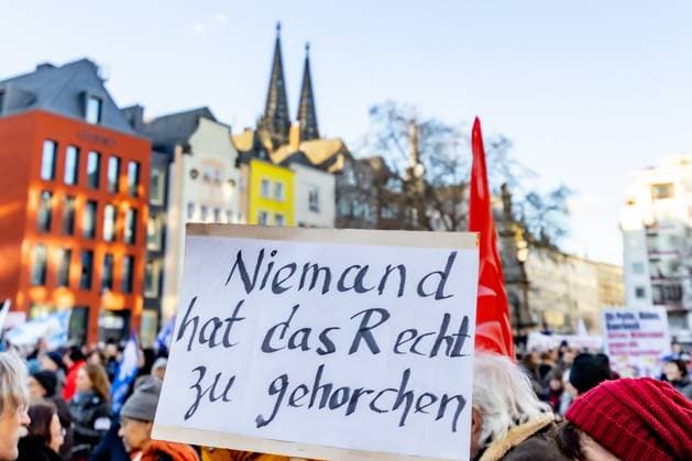 Schild: Niemand hat das Rech zu gehorchen - Aktionswochenende öStoppt das Töten für Waffenstillstand und Verhandlungen!˜ von Deutsche Friedensgesellschaft Vereinigte KriegsdienstgegnerInnen auf dem Alter Markt in Köln 25.02.2023 Köln Altstadt NRW Deutschland