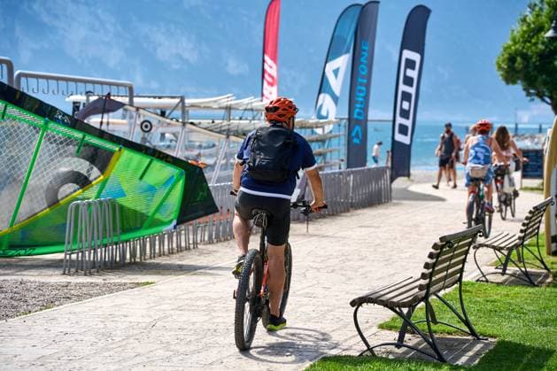 Fahrradfahrer bzw. Radfahrer fahren mit dem Fahrrad, bzw. Rad um den Gardasee und machen eine Radtour entlang des Rundwegs am See in Italien.