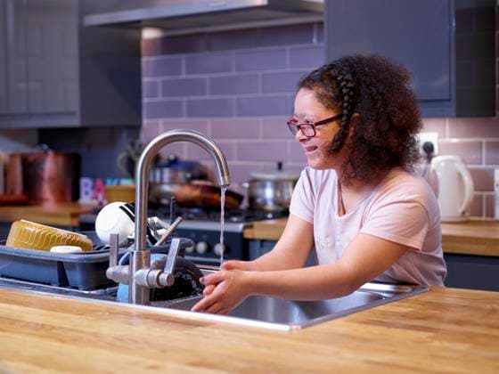 Girl with Down syndrome washing hands in kitchen sink model released Copyright: xCulturaxCreativex
