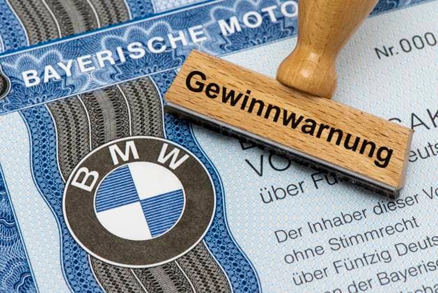 Gewinnwarnung für BMW Ein Holzstempel ist beschriftet mit dem Aufdruck: Gewinnwarnung, über einer BMW-Aktie mit Firmen-Logo Symbolbild