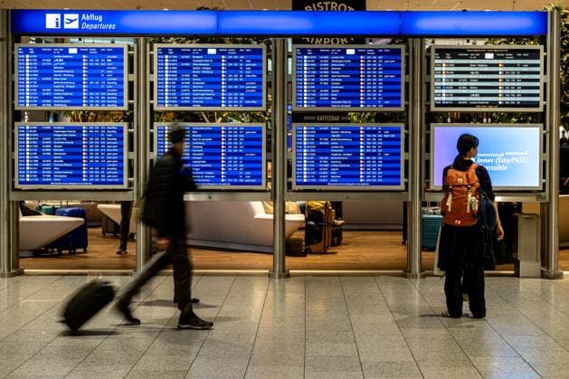 Reisende vor Abflug-Anzeigetafeln im Terminal 12.11.24, Frankfurt: Symbolfoto, Illustrationsbild, Symbolbild, Illustrationsfoto, Alltagsszene Reisende vor Abflug-Anzeigetafeln im Terminal Passagiere stehen und gehen vor einer Reihe von blauen Abflug-Anzeigetafeln im Flughafen, die Informationen zu Flugzielen, Abflugzeiten und Gates anzeigen. Eine Frau mit orangefarbenem Rucksack betrachtet die Tafeln aufmerksam, während ein weiterer Reisender mit Koffer im Vorbeigehen zu sehen ist. . . Frankfurt Hessen Germany