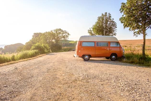 Ein Orange-weisser VW Bus Bulli steht auf einem Schotterparkplatz an einem Sommermorgen, Baden Württemberg, Deutschland. Ein Bulli steht in der Landschaft