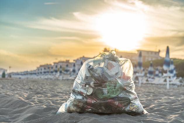 Ein gefüllter Müllsack mit Plastikabfällen liegt im Sand an einem Strand in Italien. Der Abfall zeigt die Umweltverschmutzung und das Problem von Plastikmüll in touristischen Küstenregionen