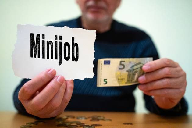 FOTOMONTAGE. Ein Mann hält ein Schild mit der Aufschrift Minijob sowie einen 5-Euro-Schein in der Hand. Minijobs spielen eine wichtige Rolle für Geringverdiener und Rentner, die ihr Einkommen aufbessern müssen.