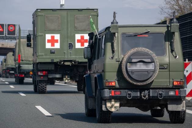 Militärfahrzeuge mit Tarnlackierung und litauischem Kennzeichen (unkenntlich) fahren auf der A9. Im Konvoi befindet sich ein Sanitätsfahrzeug mit zwei roten Kreuzen und grüner Fahne.