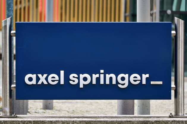Blaues Schild mit weißem axel springer Schriftzug vor dem Axel-Springer-Hochhaus in Berlin