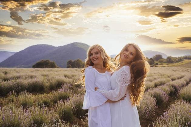 Sommerlicher Sonnenuntergang über zwei Freundinnen in weißen Kleidern, die eng beieinander in einem Lavendelfeld stehen und in den Hintergrund schauen. Verbringen Zeit zusammen nach langer Pause Summer sunset over two women friends in white dresses, standing close to each other in lavender field, looking away in back lit. Spending time together after long break Copyright: imageBROKER OksanaxShufrych ibxiqx13439911.jpg ,model released, Symbolfoto ,property released