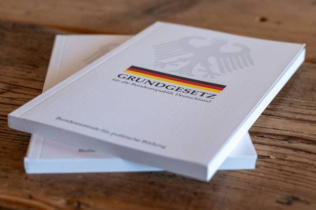 Grundgesetz der Bundesrepublik Deutschland auf Holztisch 19.06.25, Limburg: Symbolfoto, Illustrationsbild, Symbolbild, Illustrationsfoto, Alltagsszene Ein gedrucktes Exemplar des Grundgesetzes der Bundesrepublik Deutschland liegt auf einem rustikalen Holztisch. Die Ausgabe mit Bundesadler, schwarz-rot-goldenem Streifen und dem Titel Grundgesetz für die Bundesrepublik Deutschland symbolisiert demokratische Werte, Rechtsstaatlichkeit und politische Bildung in Deutschland. Im Hintergrund ist ein zweites Exemplar sichtbar. Limburg Copyright: xW2Artx xKlaraxMichelx