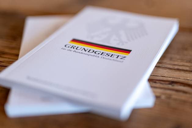 Grundgesetz der Bundesrepublik Deutschland auf Holztisch 19.06.25, Limburg: Symbolfoto, Illustrationsbild, Symbolbild, Illustrationsfoto, Alltagsszene Ein gedrucktes Exemplar des Grundgesetzes der Bundesrepublik Deutschland liegt auf einem rustikalen Holztisch. Die Ausgabe mit Bundesadler, schwarz-rot-goldenem Streifen und dem Titel Grundgesetz für die Bundesrepublik Deutschland symbolisiert demokratische Werte, Rechtsstaatlichkeit und politische Bildung in Deutschland. Im Hintergrund ist ein zweites Exemplar sichtbar. Limburg Copyright: xW2Artx xKlaraxMichelx