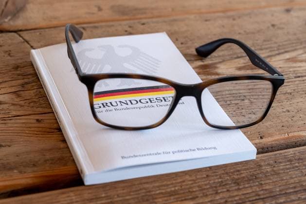 Grundgesetz der Bundesrepublik Deutschland mit Brille 19.06.25, Limburg: Symbolfoto, Illustrationsbild, Symbolbild, Illustrationsfoto, Alltagsszene Eine Brille liegt auf einem geschlossenen Exemplar des Grundgesetzes der Bundesrepublik Deutschland. Das Buch mit Bundesadler und schwarz-rot-goldenem Streifen liegt auf einem Holztisch. Die Szene steht symbolisch für reflektiertes Lesen, politische Bildung, Rechtsbewusstsein und den individuellen Zugang zu demokratischen Werten und Grundrechten. Limburg Copyright: xW2Artx xKlaraxMichelx