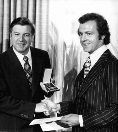Rugby Fußball Sept. 09, 1976 - Fußball-Spieler Franz Beckenbauer wurde mit dem Bundesverdienstkreuz ausgezeichnet.: Franz Beckenbauer (31), der berühmte bayerische Fußballspieler, hat am 16. September 1976 das Bundesverdienstkreuz am Bande erhalten. Der Kapitän des Fußballvereins Bayern München sowie der westdeutschen Nationalmannschaft, die seit 1974 Weltmeister ist, wurde auf Empfehlung des bayerischen Ministerpräsidenten vom Bundespräsidenten mit dem Verdienstkreuz ausgezeichnet. Das Foto zeigt Franz Beckenbauer (r) nach der Verleihung des Verdienstkreuzes durch den bayerischen Kultusminister Hans Maier (l.).