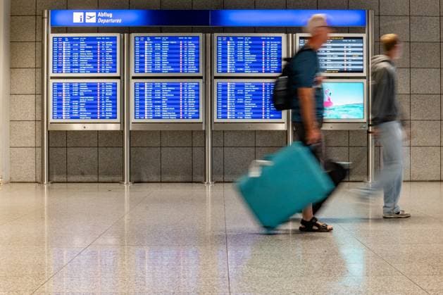 Passagiere mit Gepäck vor Abfluganzeige Flughafen Frankfurt 22.07.25, Frankfurt: Symbolfoto, Illustrationsbild, Symbolbild, Illustrationsfoto, Alltagsszene Zwei Passagiere gehen mit Gepäck an einer digitalen Abflugtafel im Frankfurter Flughafen vorbei. Einer der Reisenden zieht einen auffällig türkisfarbenen Rollkoffer. Im Hintergrund sind aktuelle Flugverbindungen sowie eine touristische Werbeanzeige zu sehen. Die Aufnahme verbindet Bewegung und Information und symbolisiert typische Momente im internationalen Reiseverkehr. Frankfurt Hessen Deutschland Copyright: xW2Artx xThorstenxWagnerx