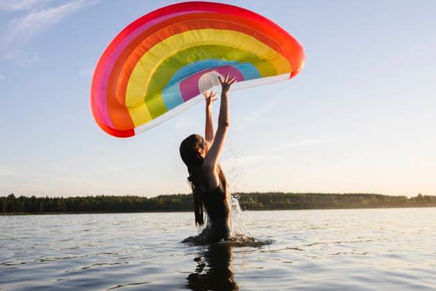 Person in swim suit playing with rainbow float in lake during summer model released, Symbolfoto, EYAF03494