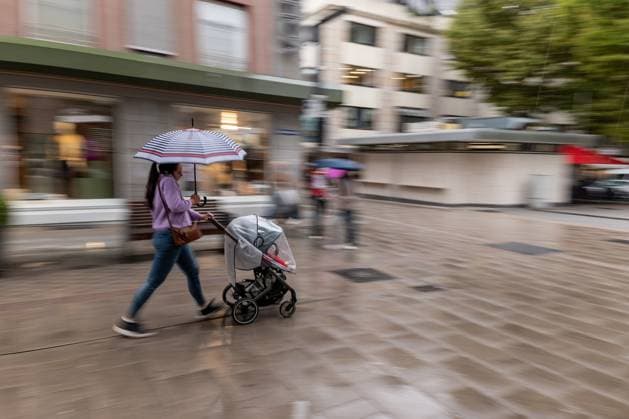 Frau mit Kinderwagen im Regen 09.09.25, Limburg: Symbolfoto, Illustrationsbild, Symbolbild, Illustrationsfoto, Alltagsszene Eine Frau schiebt mit einem Kinderwagen durch eine nasse Einkaufsstraße. Sie hält einen bunten Regenschirm und bewegt sich zügig, während die Umgebung in Bewegungsunschärfe verschwimmt. Das Bild zeigt eine Alltagsszene bei Regenwetter in urbaner Umgebung. Limburg Hessen Deutschland Copyright: xThorstenxWagnerx