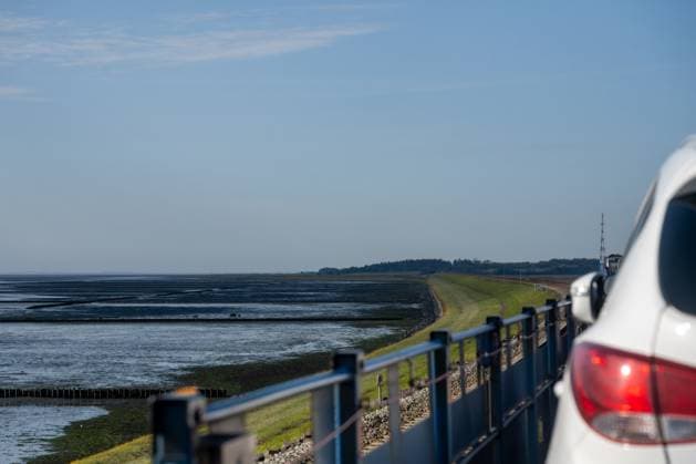 Reise auf die Insel Sylt. Blick vom Autotransportwagen auf den Hindenburgdamm in Richtung der Insel Sylt in einer Linkskurve bei Ebbe. Am rechten Rand angeschnitten ein PKW. Nordfriesland Schleswig-Holstein Deutschland