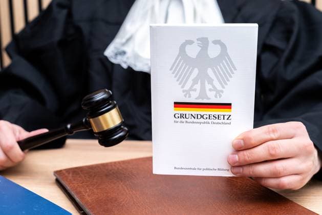 Ein Richter hält das Grundgesetz der BRD in der Hand. Das Symbolfoto steht für Rechtsstaat, Verfassung, Demokratie und die Bedeutung der Grundgesetze in der Bundesrepublik Deutschland