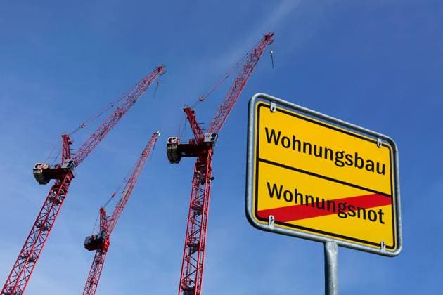 Baukräne und Ortsschild mit Schriftzüge Wohnungsbau sowie Wohnungsnot Fotomontage: Baukräne und Ortsschild mit Schriftzüge Wohnungsbau sowie Wohnungsnot, 13.10.2025, Neben mehreren Baukränen befindet sich ein Ortsschild mit den Schriftzügen Wohnungsbau sowie Wohnungsnot.