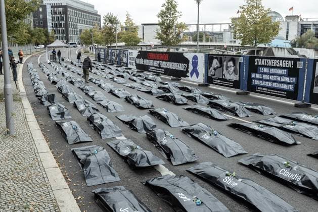 Protestaktion der Patientenorganisation Kinder ME CFS vorm Bundesministerium für Forschung, Technologie und Raumfahrt. Deutschland, Berlin am 15.10.2025: 100 Leichensäcke vor dem BMFTR als stille Visualisierung der humanitären Katastrophe (Zitat). Schwarzer Leichensack mit Vornamen und dem Banner im Hintergrund ME CFS, Long Covid, Post Vac: Lebendig begraben. Frau Bär: Wo bleibt Merz Forschungsdekade?