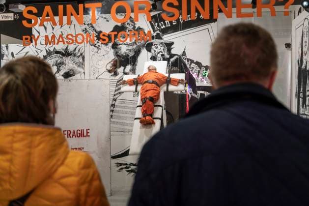 November 8, 2025, Basel, Basel-Stadt, Switzerland: People looking at a sculpture depicting the US President Donald Trump in a prisoner orange jumpsuit and strapped to a cross looking like a death row strapped-down bed, is displayed in a gallery of the city centre of Basel, Switzerland Basel Switzerland - ZUMAp199 20251108_zip_p199_013 Copyright: xMatteoxPlacuccix