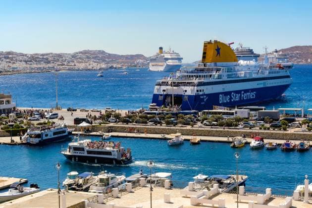Mykonos, Kykladen, Griechenland - Mykonos New Port, eine Faehre der Blue Star Ferries liegt am Kai im neuen Hafen vor der Skyline von Mykonos-Stadt. Vorne ein Taxi-Boot ein Sea Bus bringt die Touristen in die Altstadt. Hinten weitere Kreuzfahrtschiffe liegen in der Bucht vor Mykonos-Stadt mit Blick auf die Altstadt mit den Windmuehlen. Tenderboote bringen die Touristen in die Altstadt. Mykonos Mykonos Griechenland