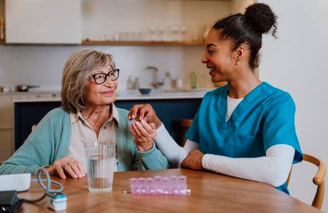 Caregiver gently explaining medication to senior with pill box at home model released, Symbolfoto property released, OIPF04840