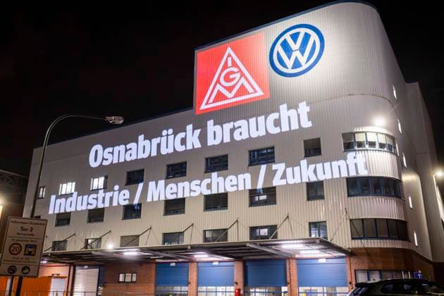 Projektion IG Metall Logo und Schriftzug Osnabrück braucht Industrie Menschen Zukunft neben dem VW Logo an der Fassader des Osnabrücker VW-Werks. Friedliche Protestkundgebung der IG Metall in Osnabück mit zur Situation Automobilbranche VW-Werk Osnabrück. 08.12.2025 IG Metall Kundgebung vor dem VW-Werk Osnabrück