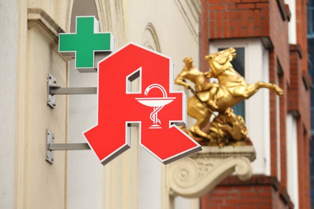Ein Apotheken-A hängt an der Fassade einer Apotheke in der Langen Reihe. Dahinter ist eine Goldskulptur an die Fassade angebracht worden. St. Georg Hamburg