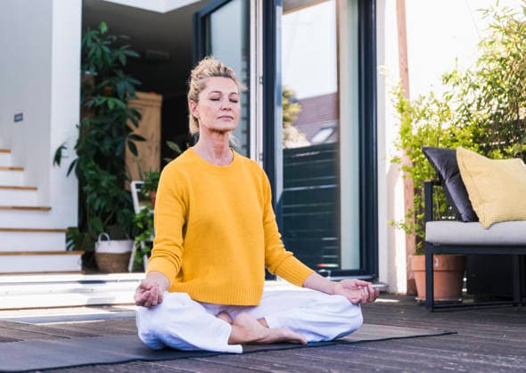 Woman meditating outdoors on sunny home terrace in yellow sweater model released, Symbolfoto property released, UUF36563
